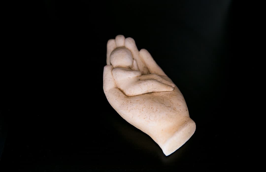 Une sculpture en pierre claire : une main qui berce un enfant endormi